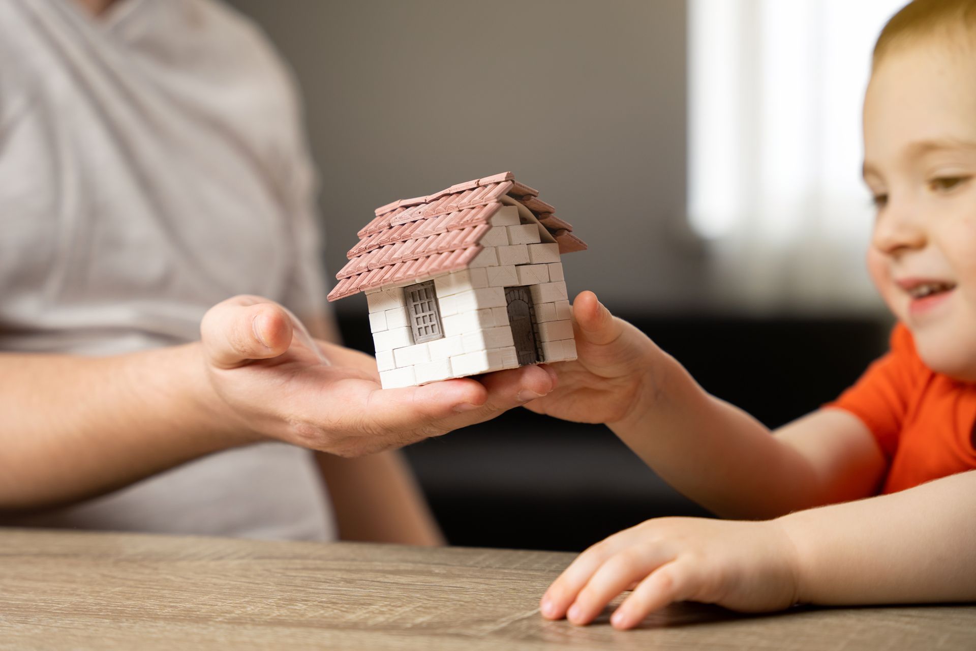 Adult and child sharing a small model house across a table indoors