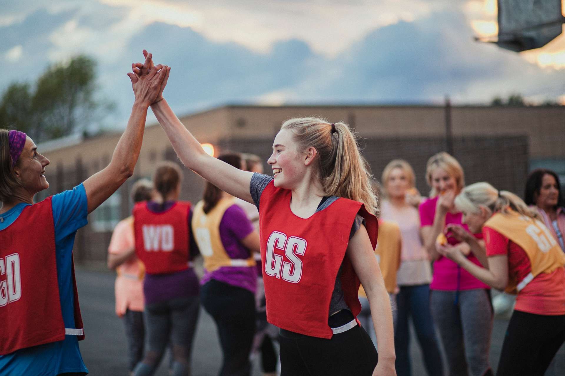 Two athletes in red bibs high-five on court, other players in background.