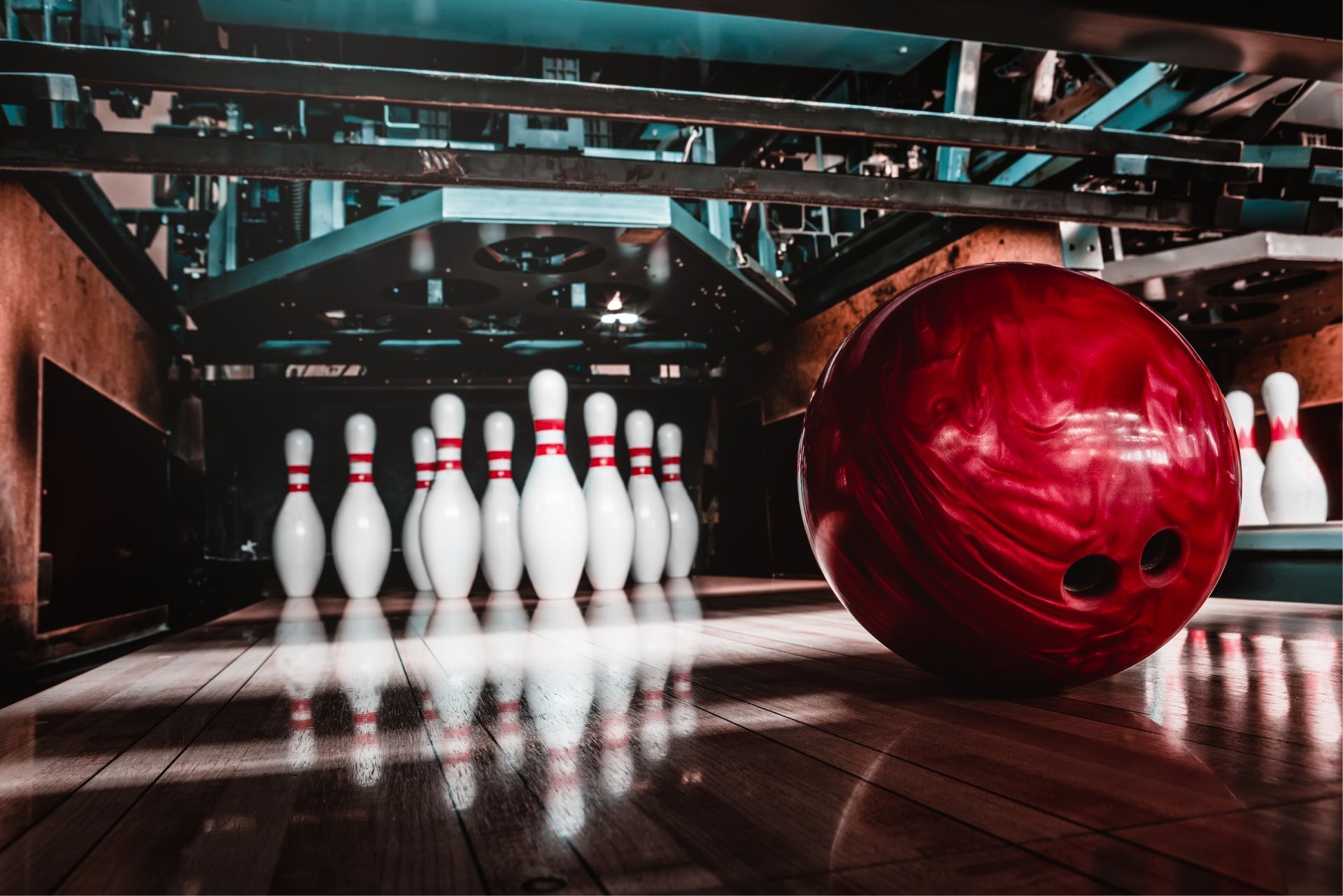 Red bowling ball rolling toward pins on a wooden lane.