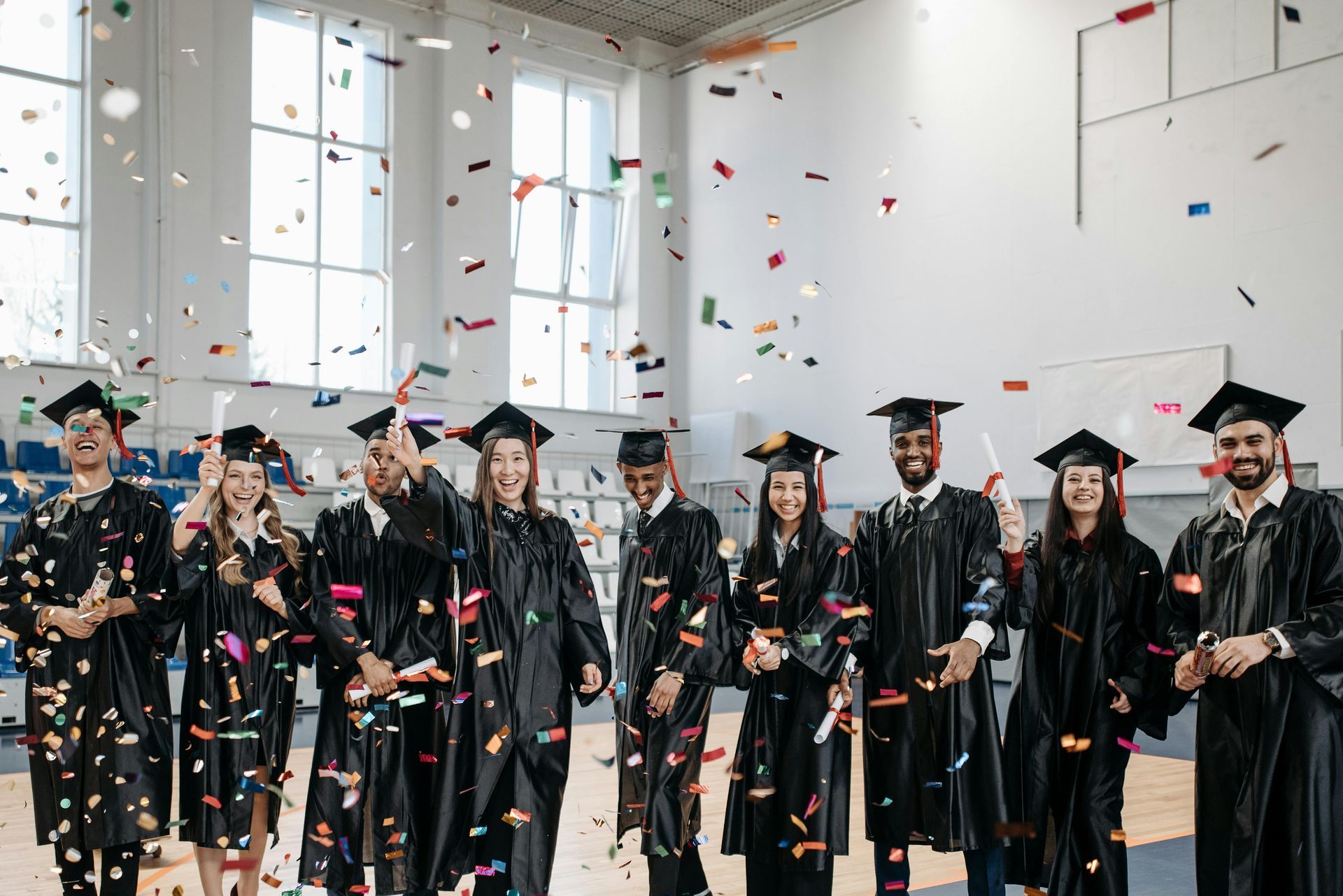 Smiling graduates in a gym with confetti