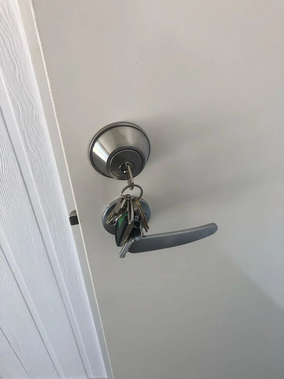A Door Handle with A Set of Keys Hanging from It. the Door and Handle Are a Light Color — Suresafe Locksmiths in Glenvale, QLD