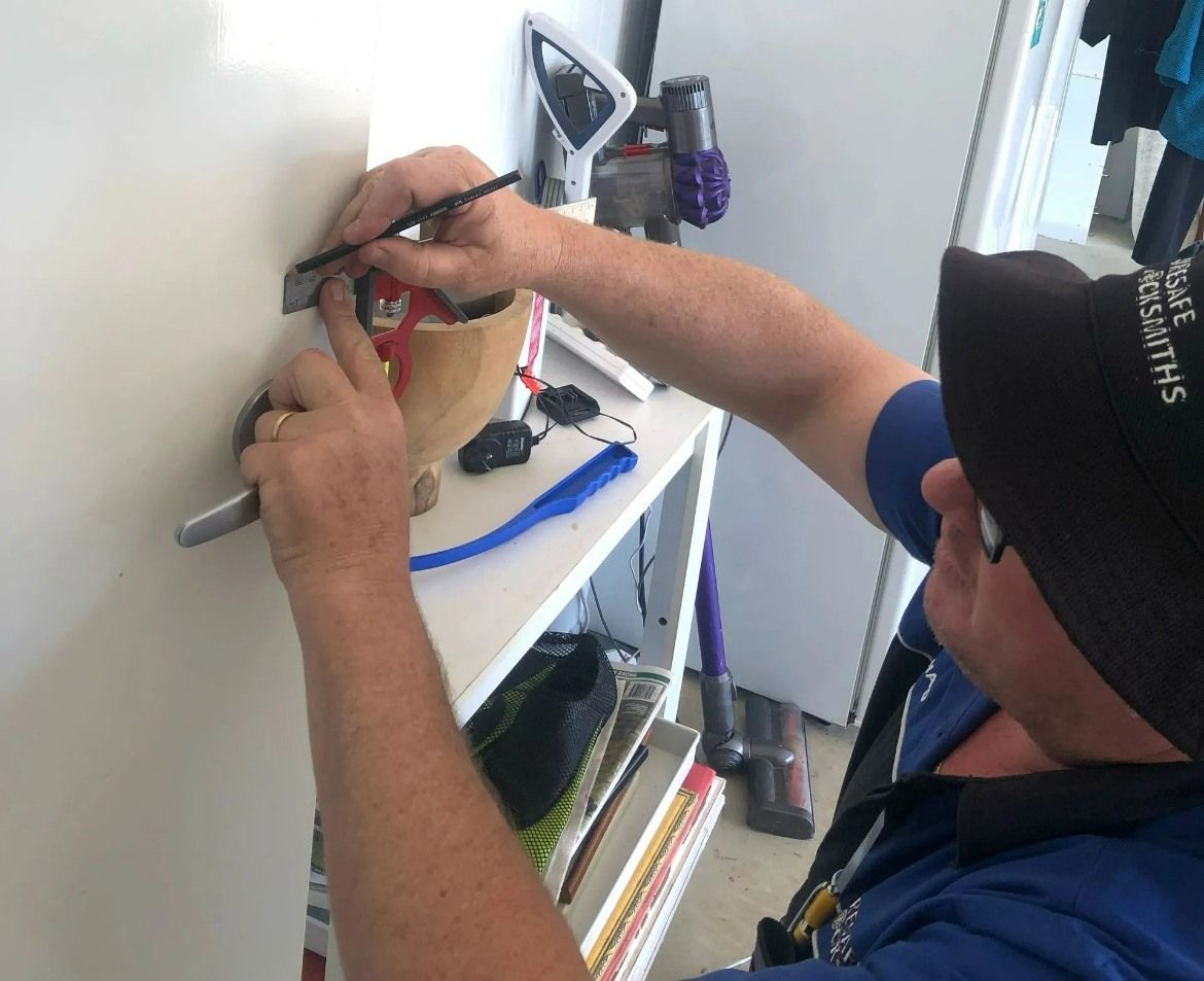 A Man is Fixing a Door Lock With a Screwdriver — Suresafe Locksmiths in Oakey, QLD