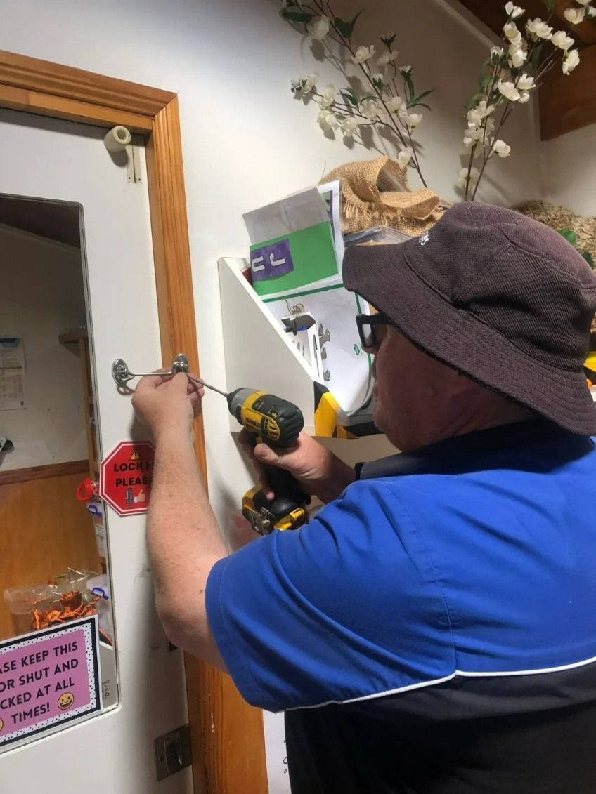 A Man in a Hat is Using a Drill to Fix a Door — Suresafe Locksmiths in Highfields, QLD