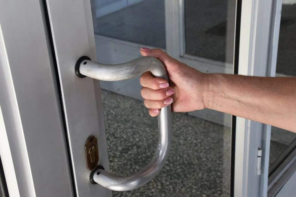 Close-up of a person’s hand holding a curved metal handle on a glass door with a visible lock.