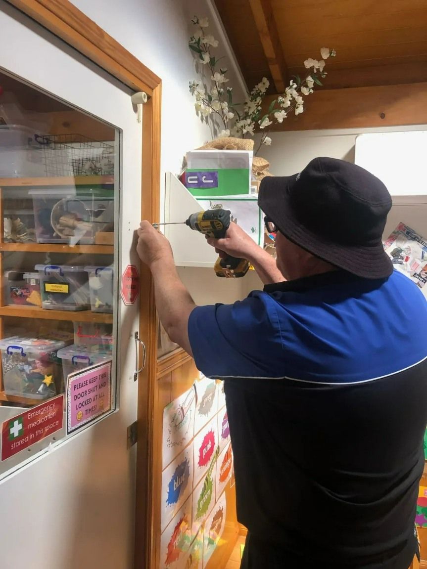 A Man is Using a Drill to Fix a Door — Suresafe Locksmiths in Glenvale, QLD