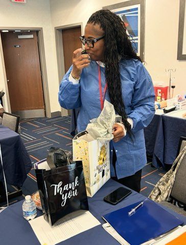 Woman at a table holding a gift bag and touching her nose, with a blue notebook and phone nearby.