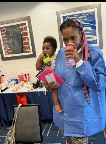 Woman in a blue gown holding a child in a clinic room, both drinking from bottles.