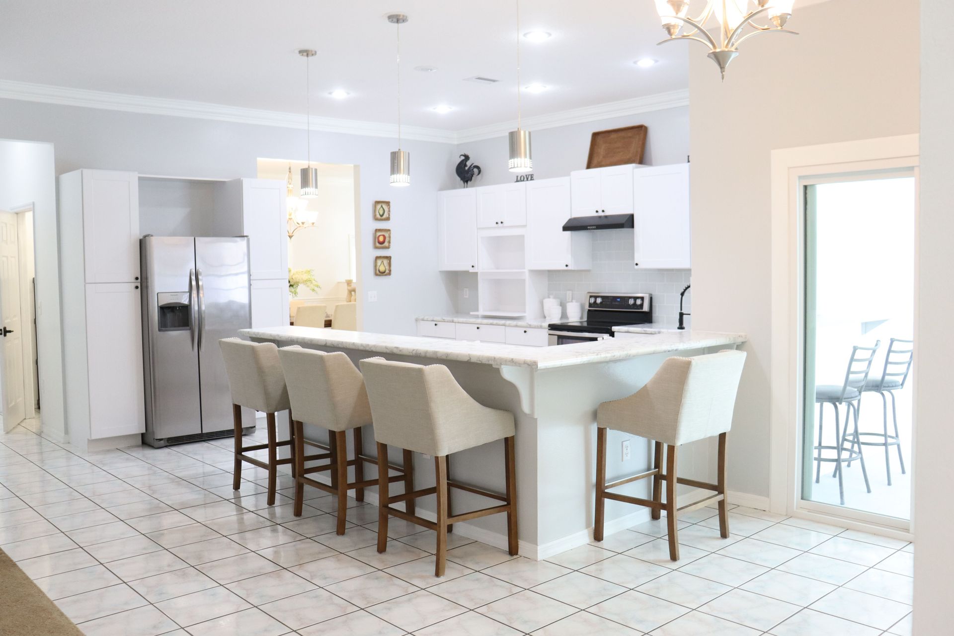 Bright white kitchen with island, bar stools, stainless fridge, and tile floor