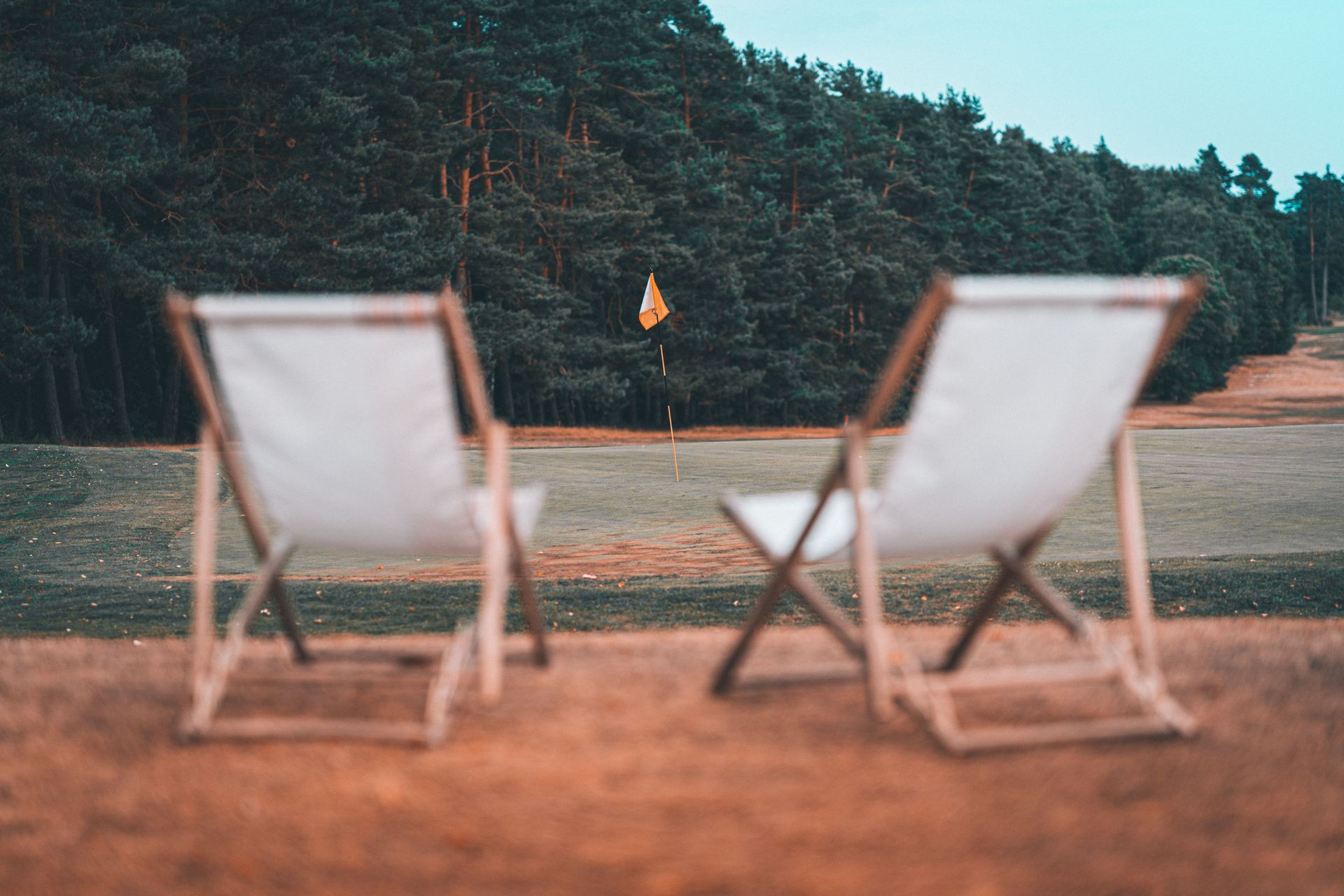 Two white deck chairs on a sandy beach facing the ocean with a forested shoreline in the background