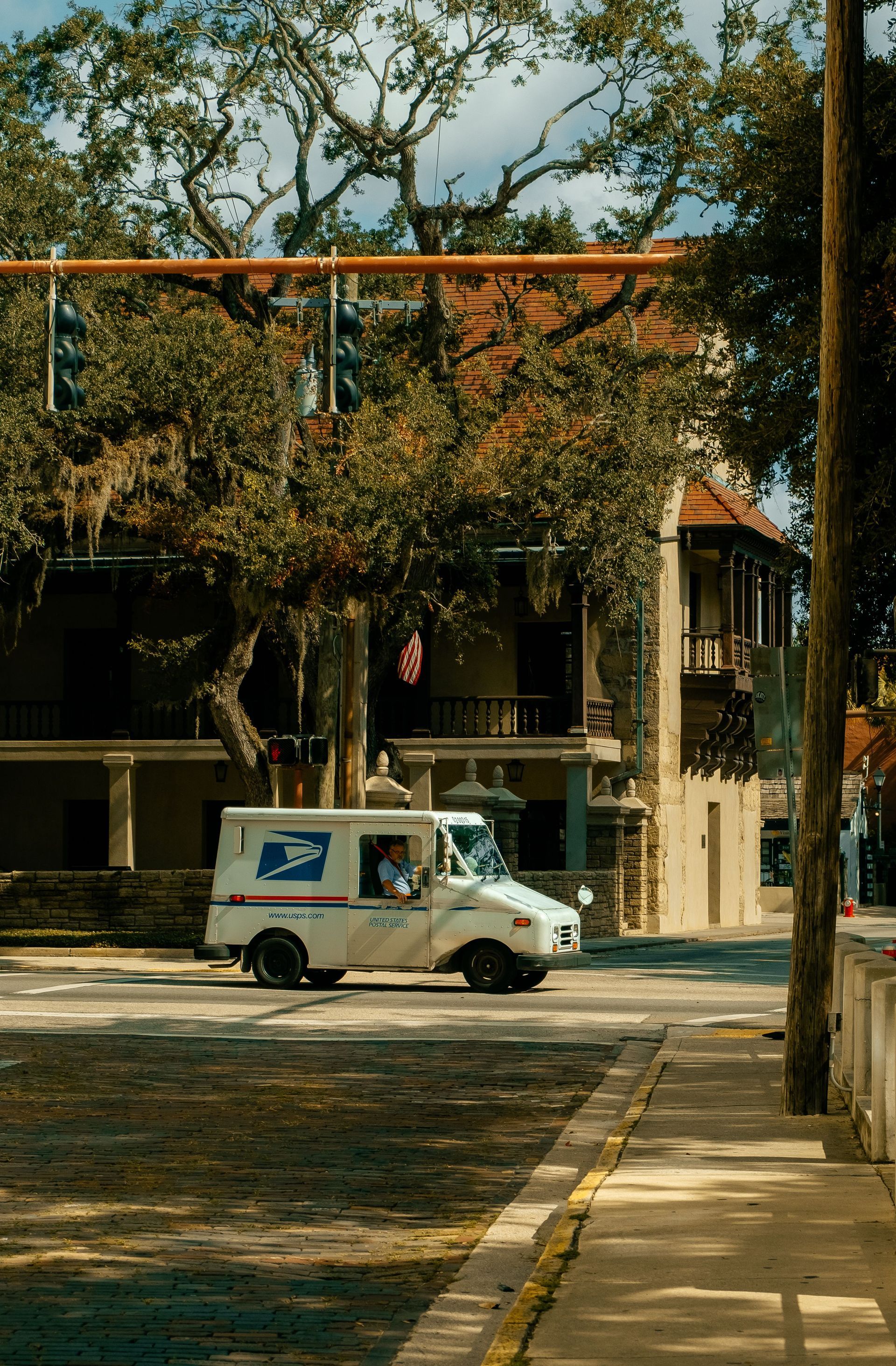 USPS mail truck parked on a tree-lined street in front of a two-story building