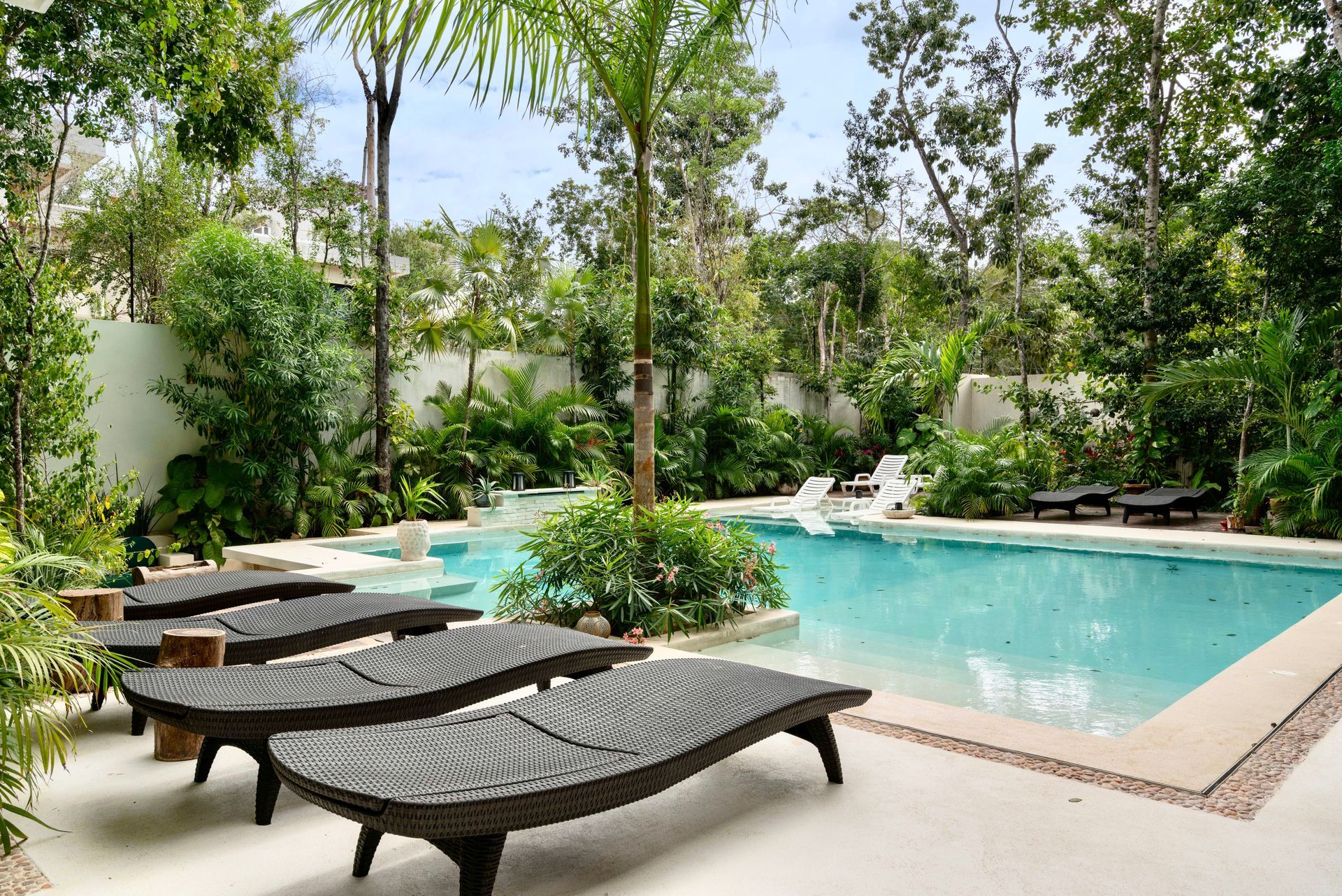 Tropical pool with turquoise water, lounge chairs, and lush green trees surrounding a patio