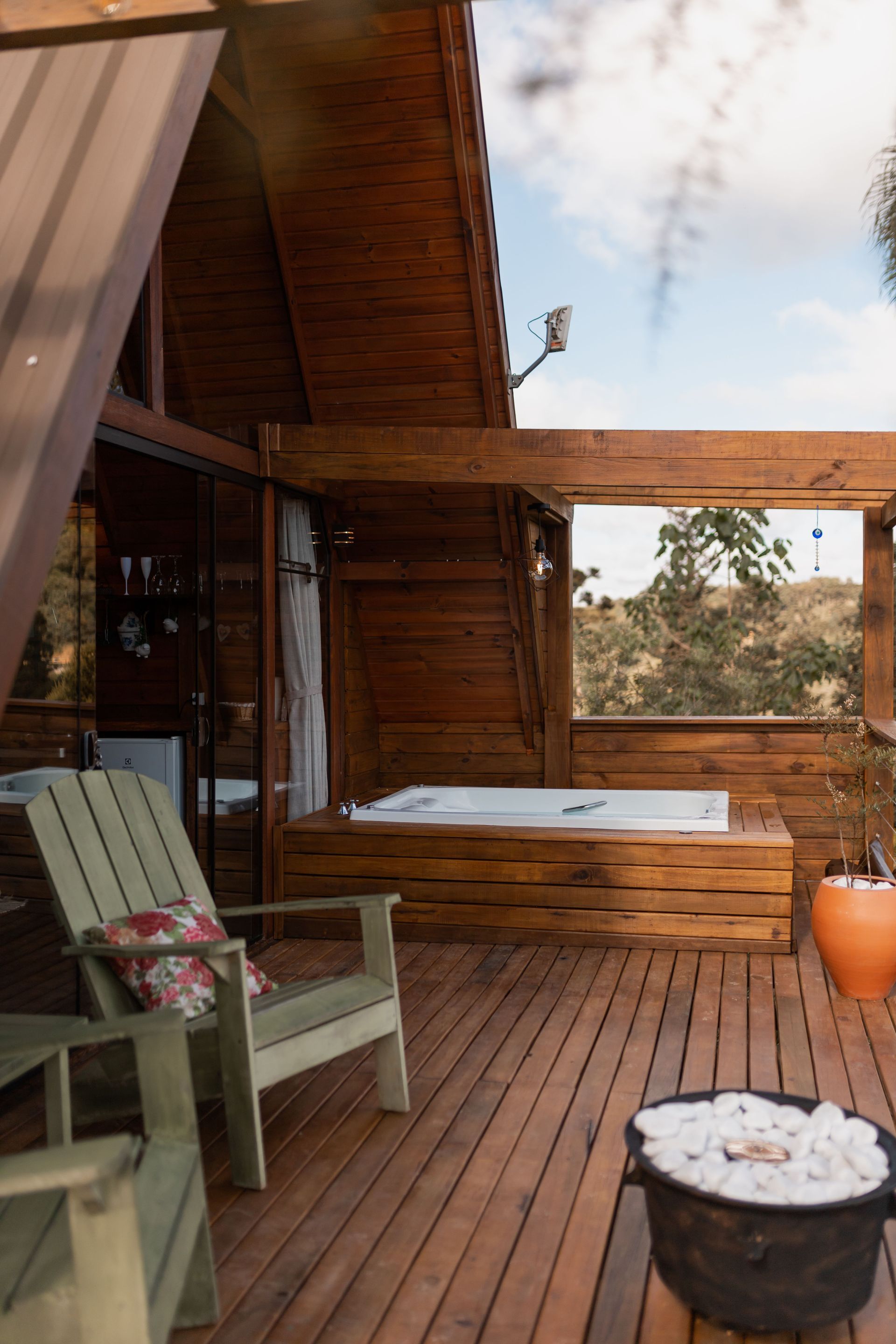 Wooden cabin porch with two chairs, a small table, and a wood-fired hot tub overlooking trees