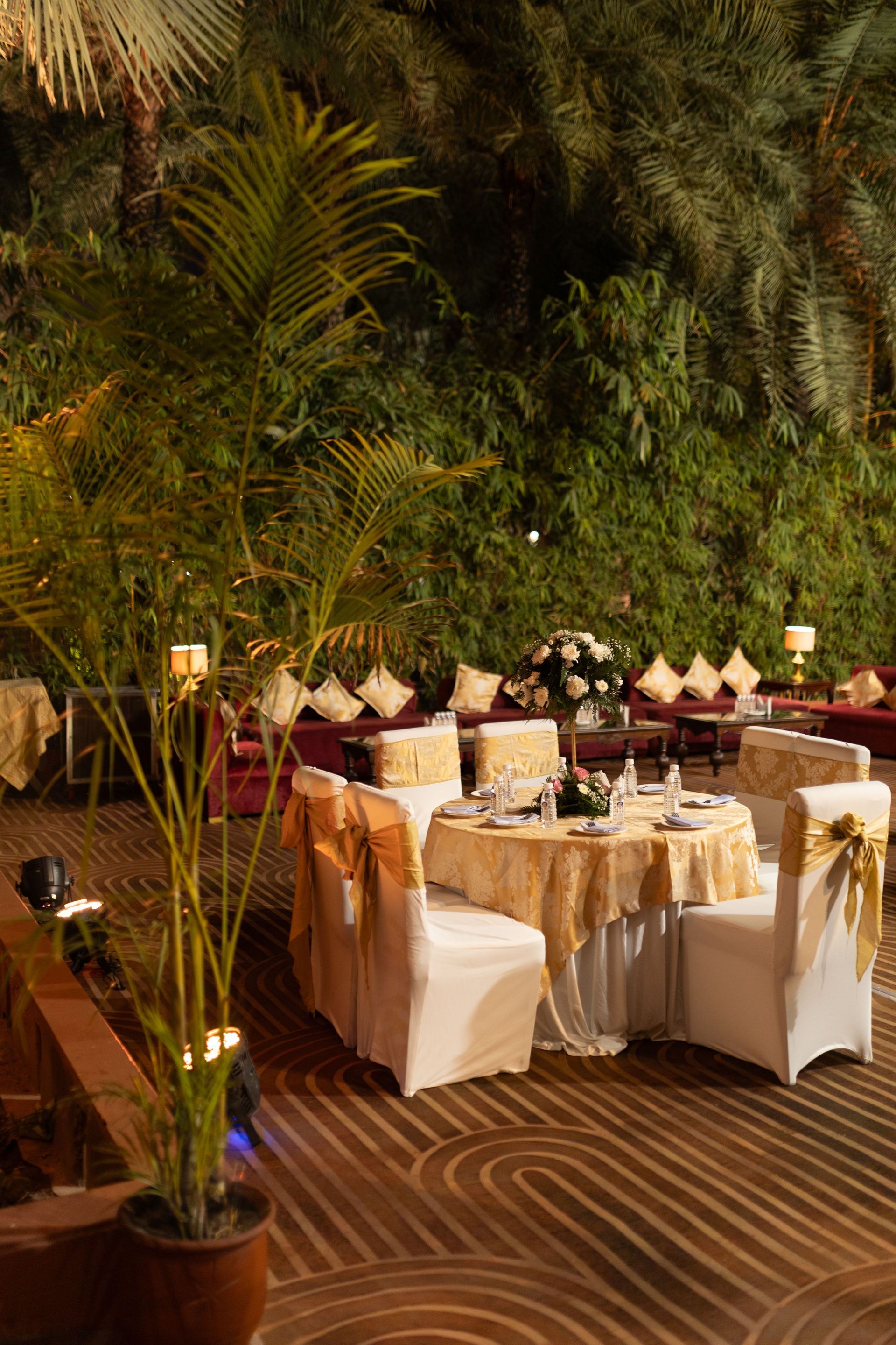 Outdoor dining tables set on a striped deck amid lush tropical greenery, softly lit with lanterns.