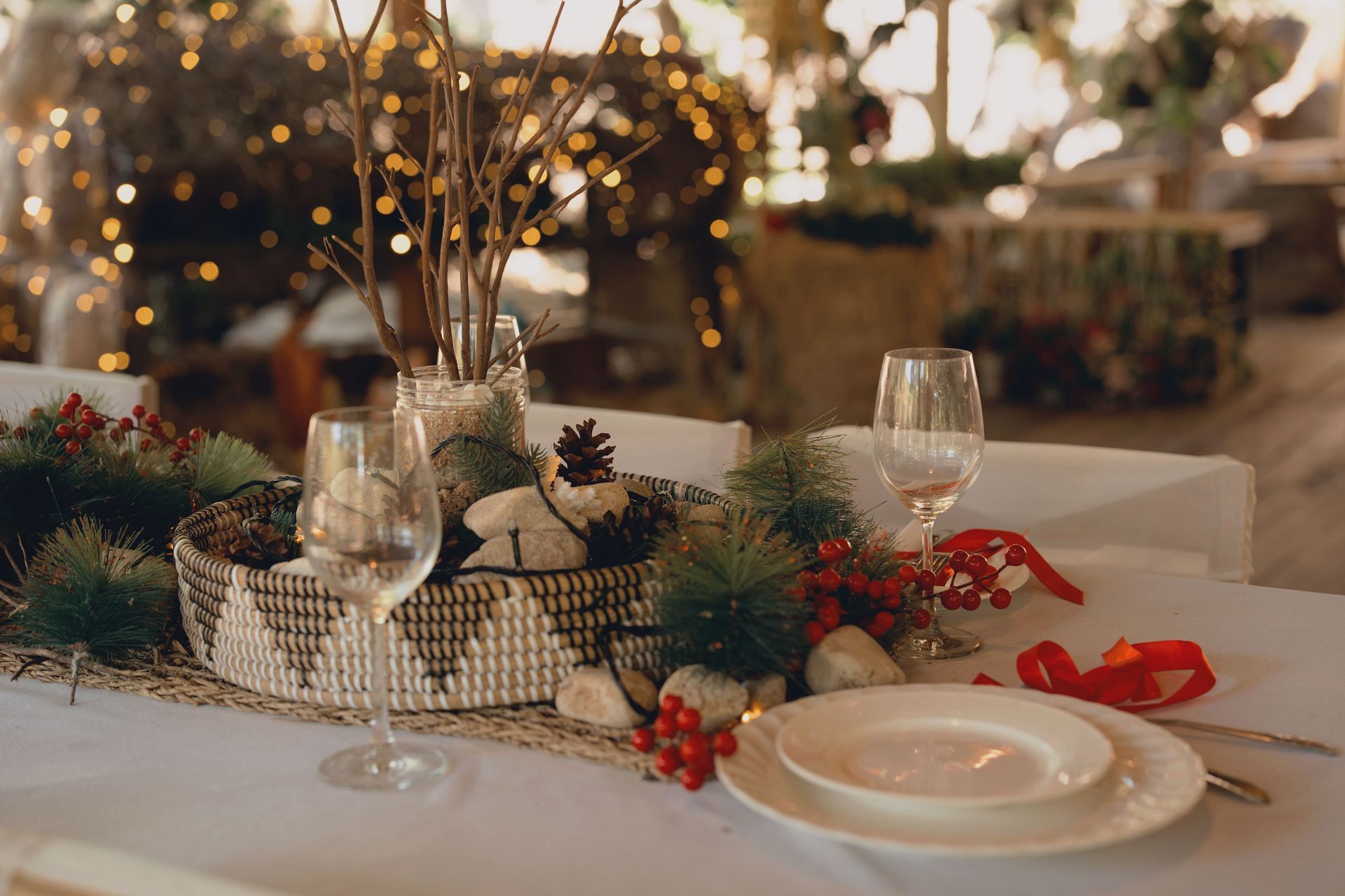 Elegant holiday table setting with candles, pinecones, wine glasses, and red berry accents