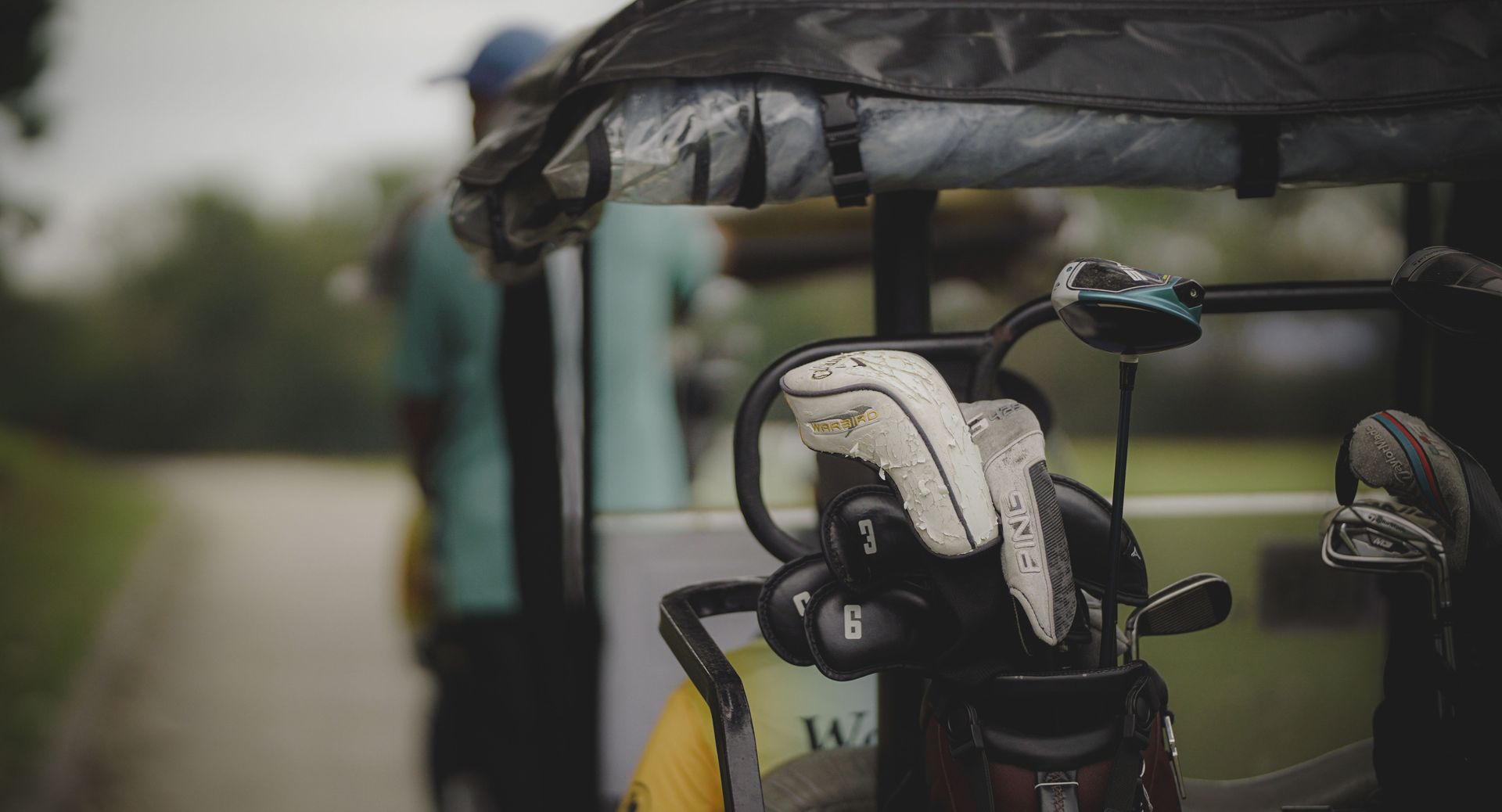 Golf bag with clubs on a cart, including a white club head cover, outdoors on a golf course