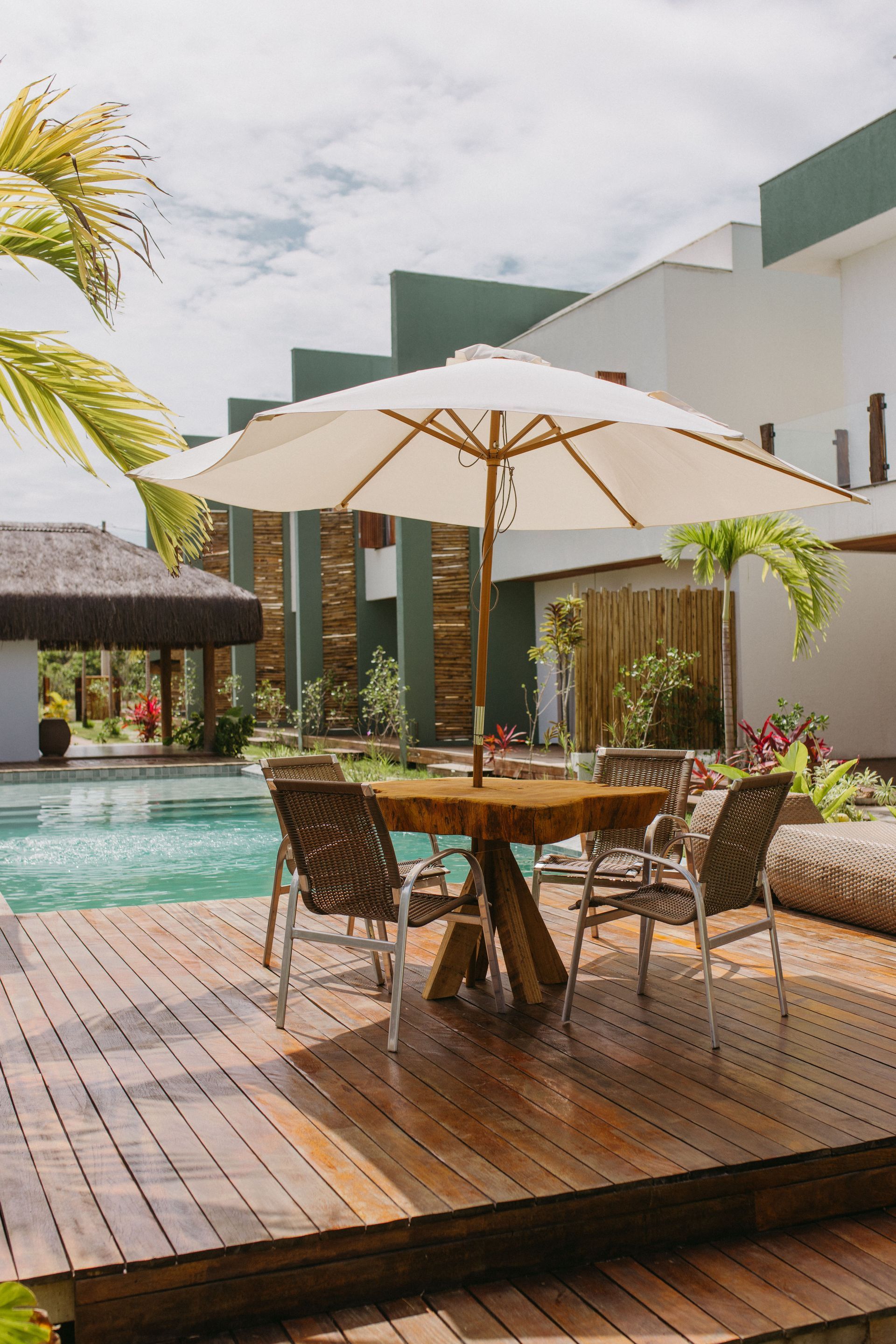 Poolside dining table with white umbrella on a wooden deck beside a modern resort pool