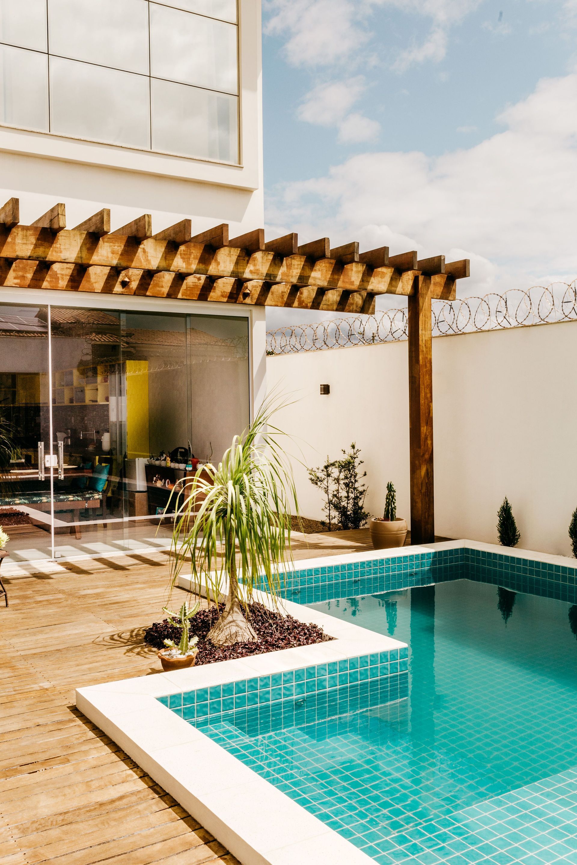 Modern patio with turquoise tiled pool, wooden deck, and shaded outdoor seating area