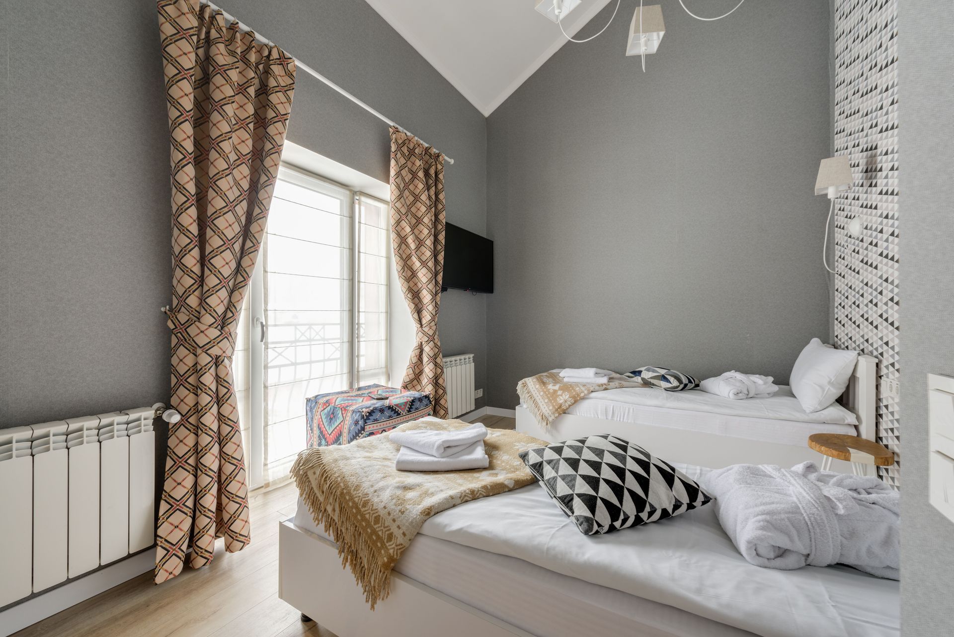 Bright bedroom with a bed, gray walls, patterned curtains, and a window seat by French doors