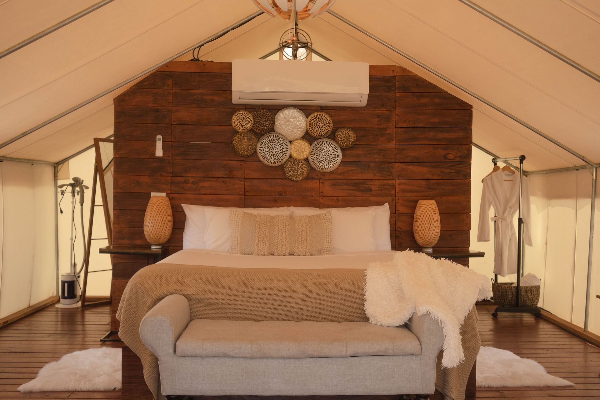 Luxury tent bedroom with a large bed, wood accent wall, chandelier, and neutral decor