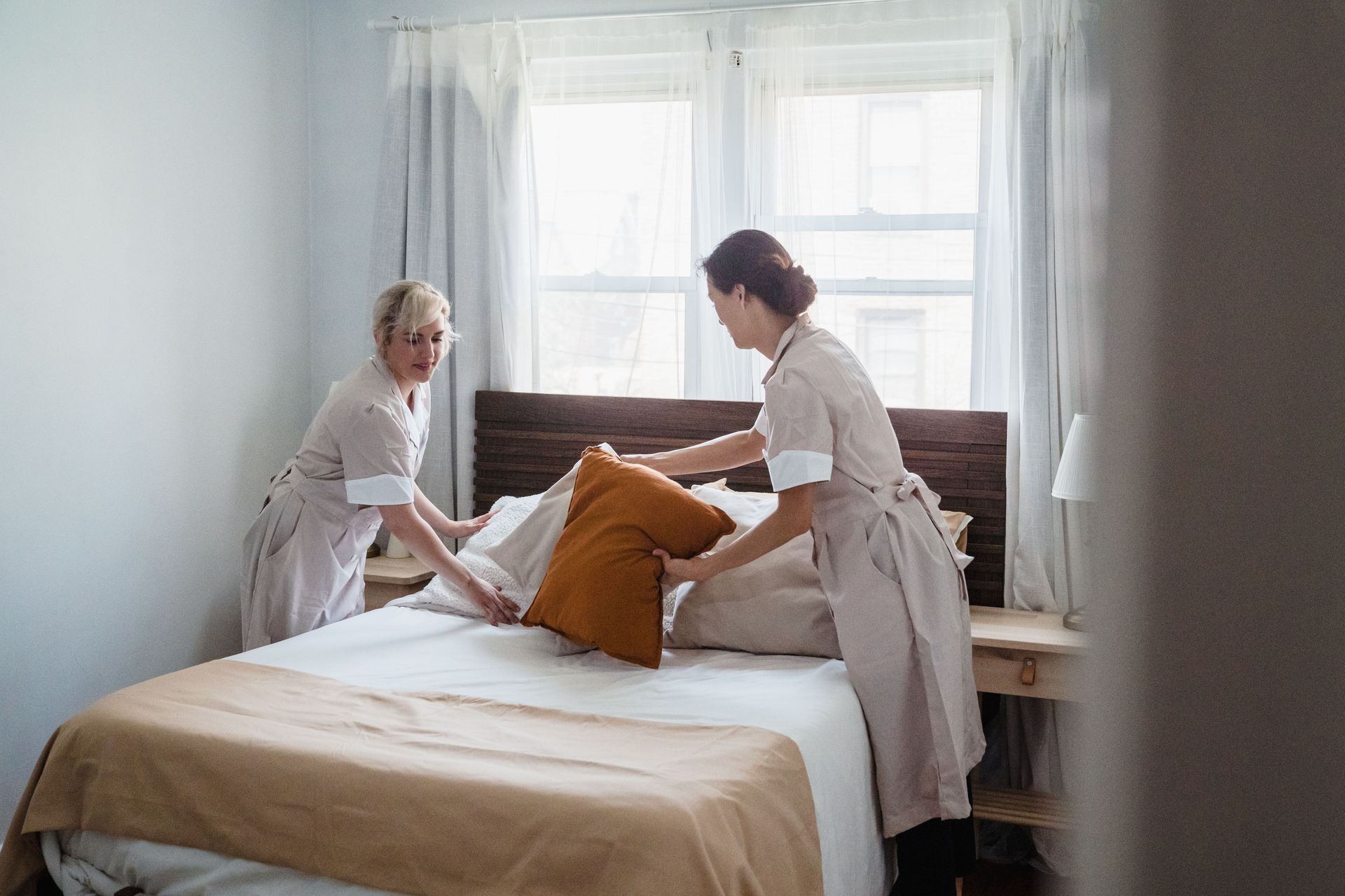 Two women making a bed in a bright, minimalist bedroom