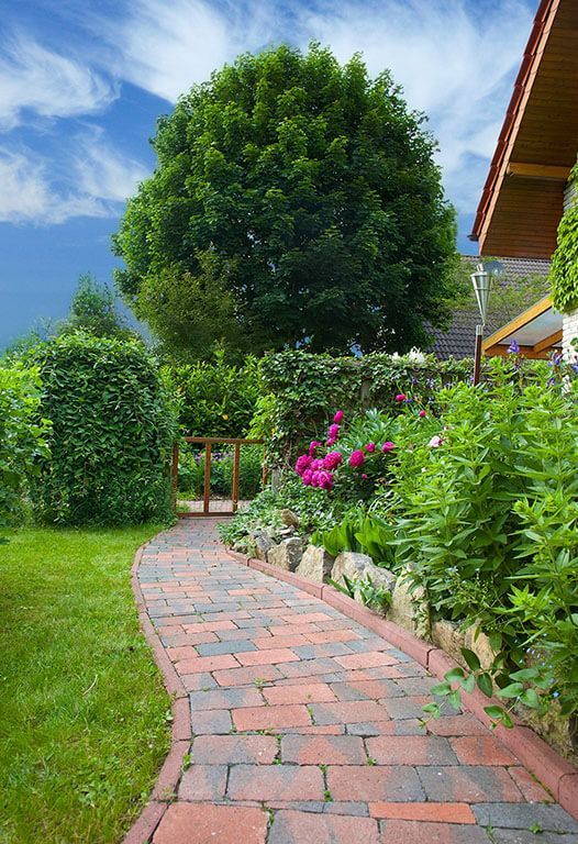 A brick walkway leading to a house in a garden.