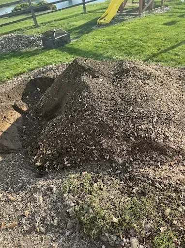 Pile of dirt and gravel beside a yard, with a yellow slide in the background.