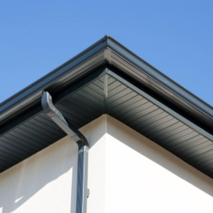 Close-up of a house roof corner with gray gutters against a blue sky