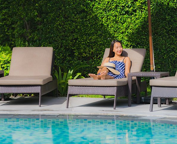 Woman relaxing on a lounge chair beside a turquoise pool with green hedge backdrop