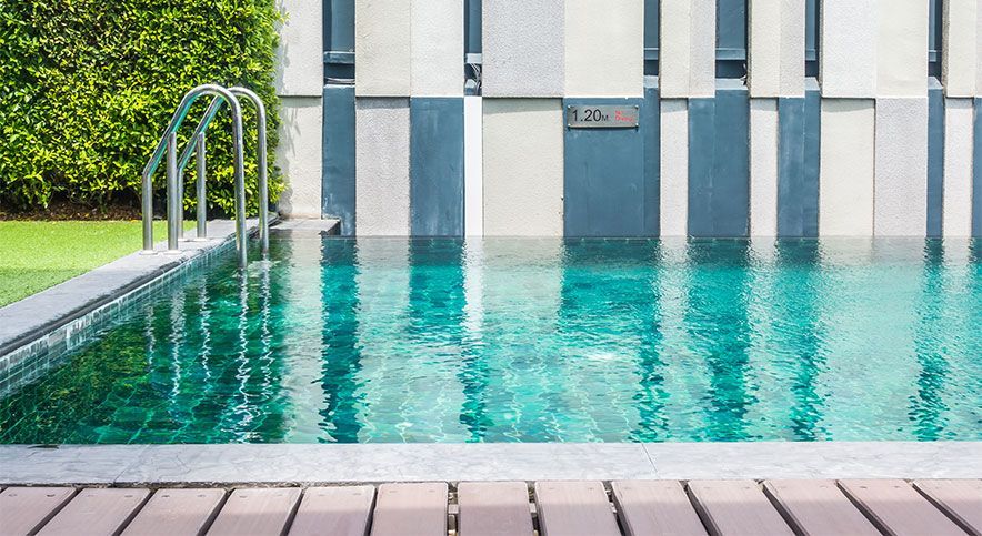 Outdoor swimming pool with turquoise water beside a modern tiled wall and wooden deck