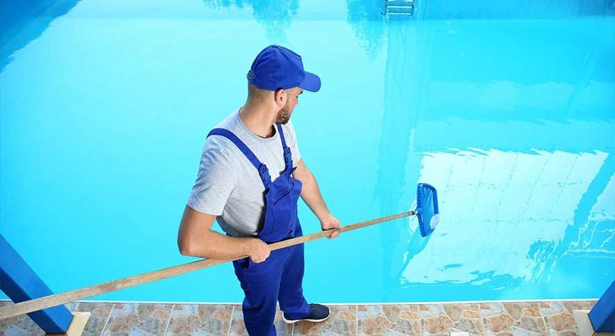 Worker in blue overalls cleaning a swimming pool with a long-handled brush