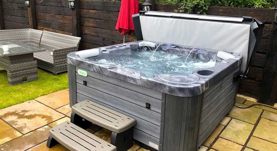 Outdoor hot tub with bubbling water on a patio beside gray seating and a red umbrella