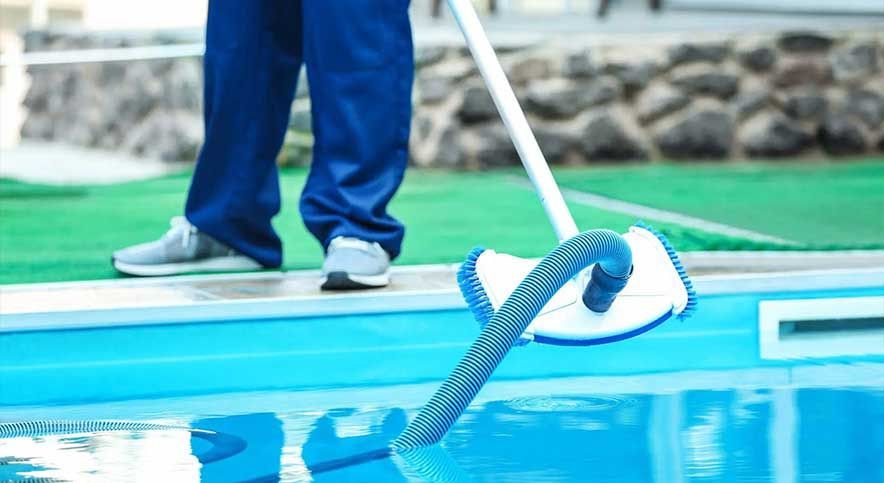 Blue pants and sneakers on a pool deck beside a coiled hose over the water