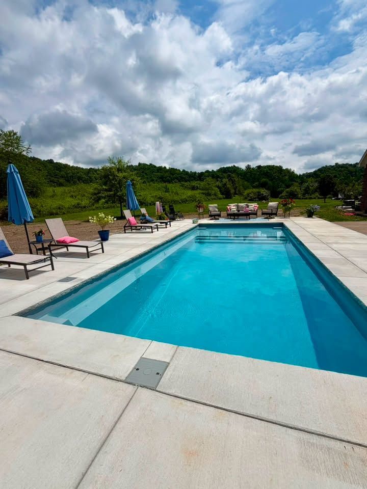 Outdoor swimming pool with blue water, lounge chairs, and umbrellas under a cloudy sky.