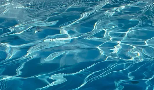 Blue swimming pool water with bright sunlight reflections and rippling waves