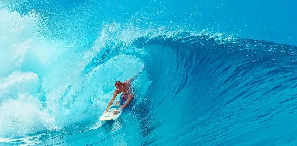 Surfer riding a blue wave inside a curling ocean barrel