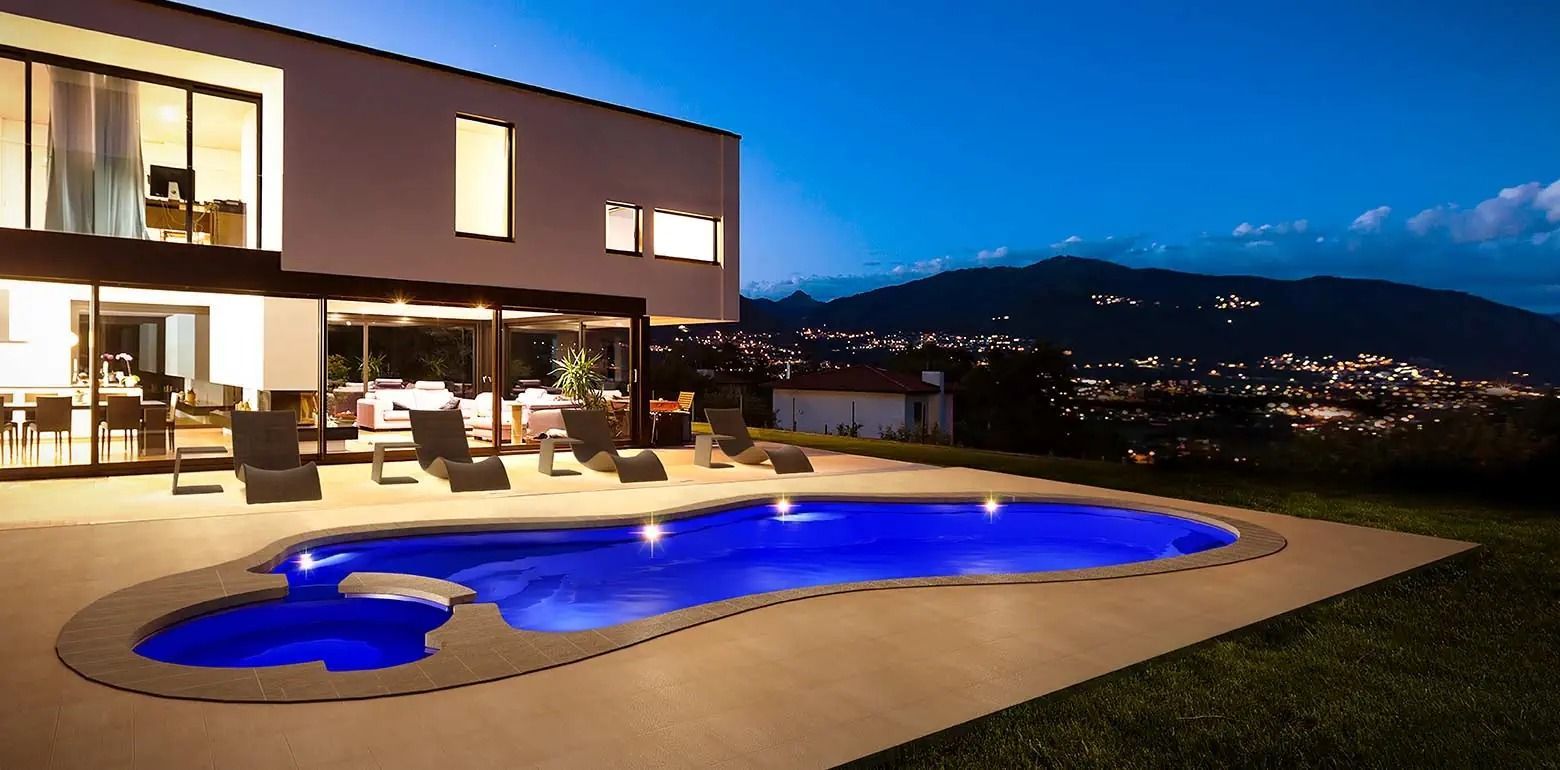 Modern house with glowing blue-lit pool at dusk overlooking city lights