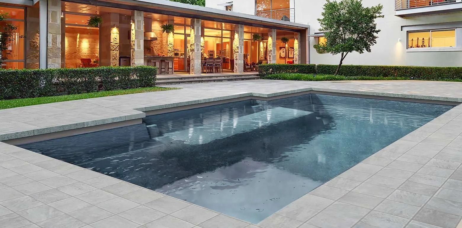 Modern backyard pool beside a glass-walled house at dusk