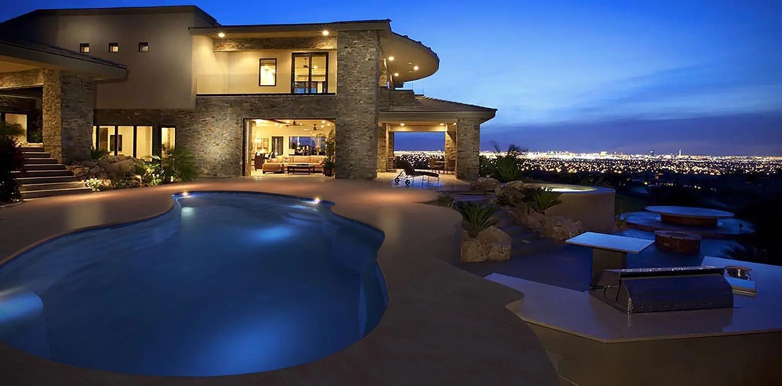 Modern luxury home at dusk with lit pool, patio, and city lights in the background