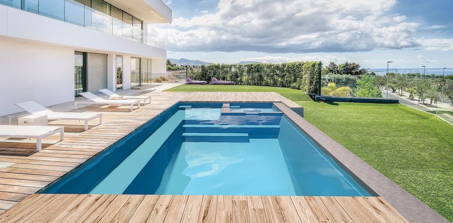 Modern villa patio with blue swimming pool, lounge chairs, and green lawn under a cloudy sky