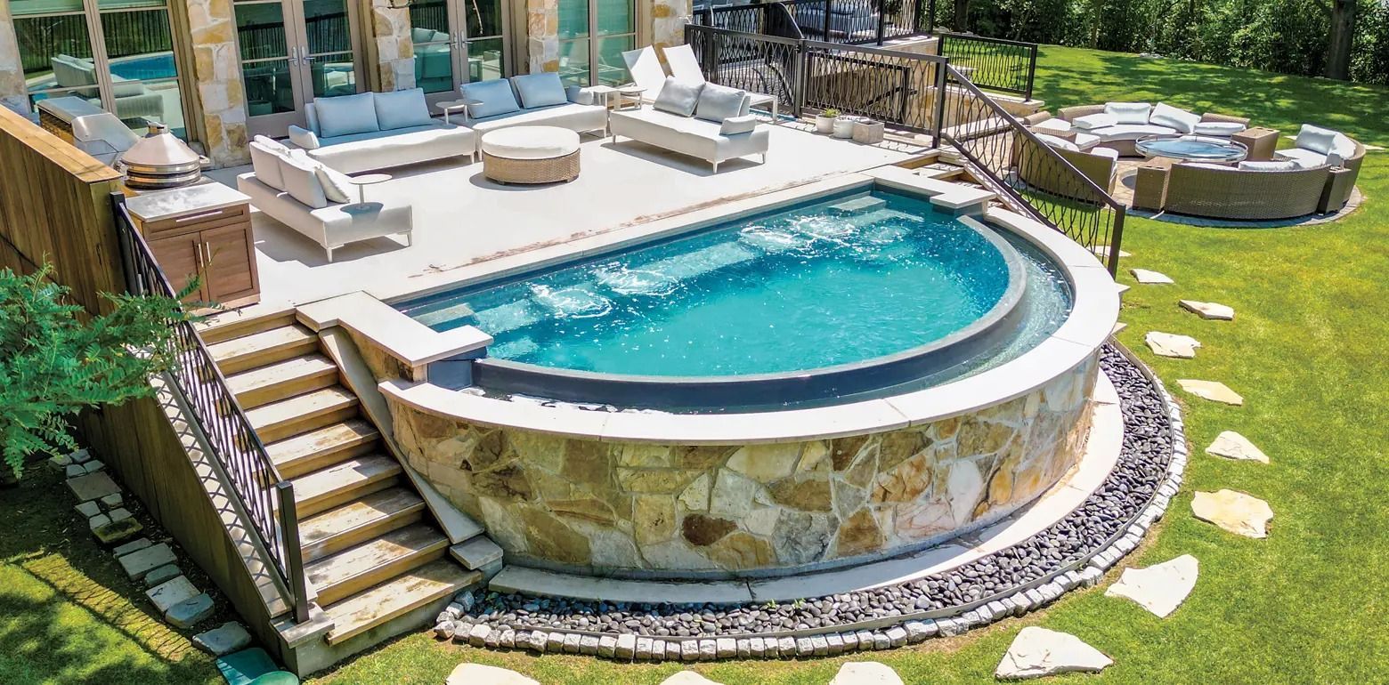 Curved in-ground swimming pool with stone patio, stairs, and grassy backyard landscaping