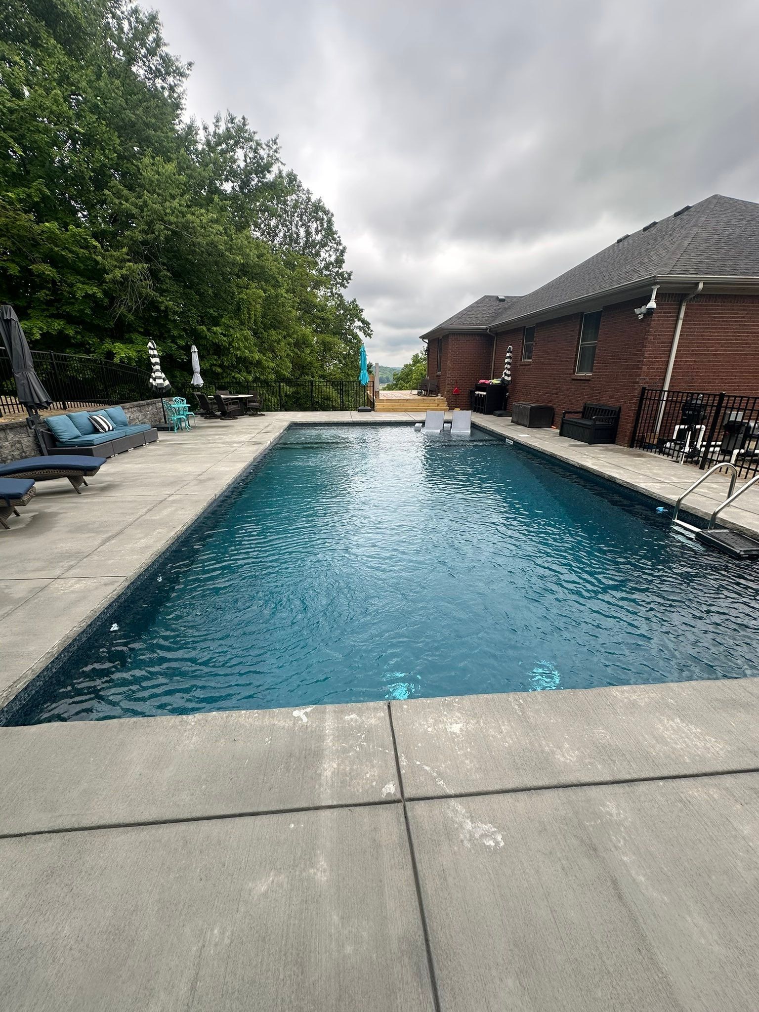 Backyard swimming pool beside a brick house under a cloudy sky