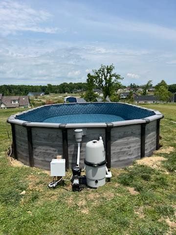 Above-ground pool in a grassy backyard with a filtration system and suburban houses in the background