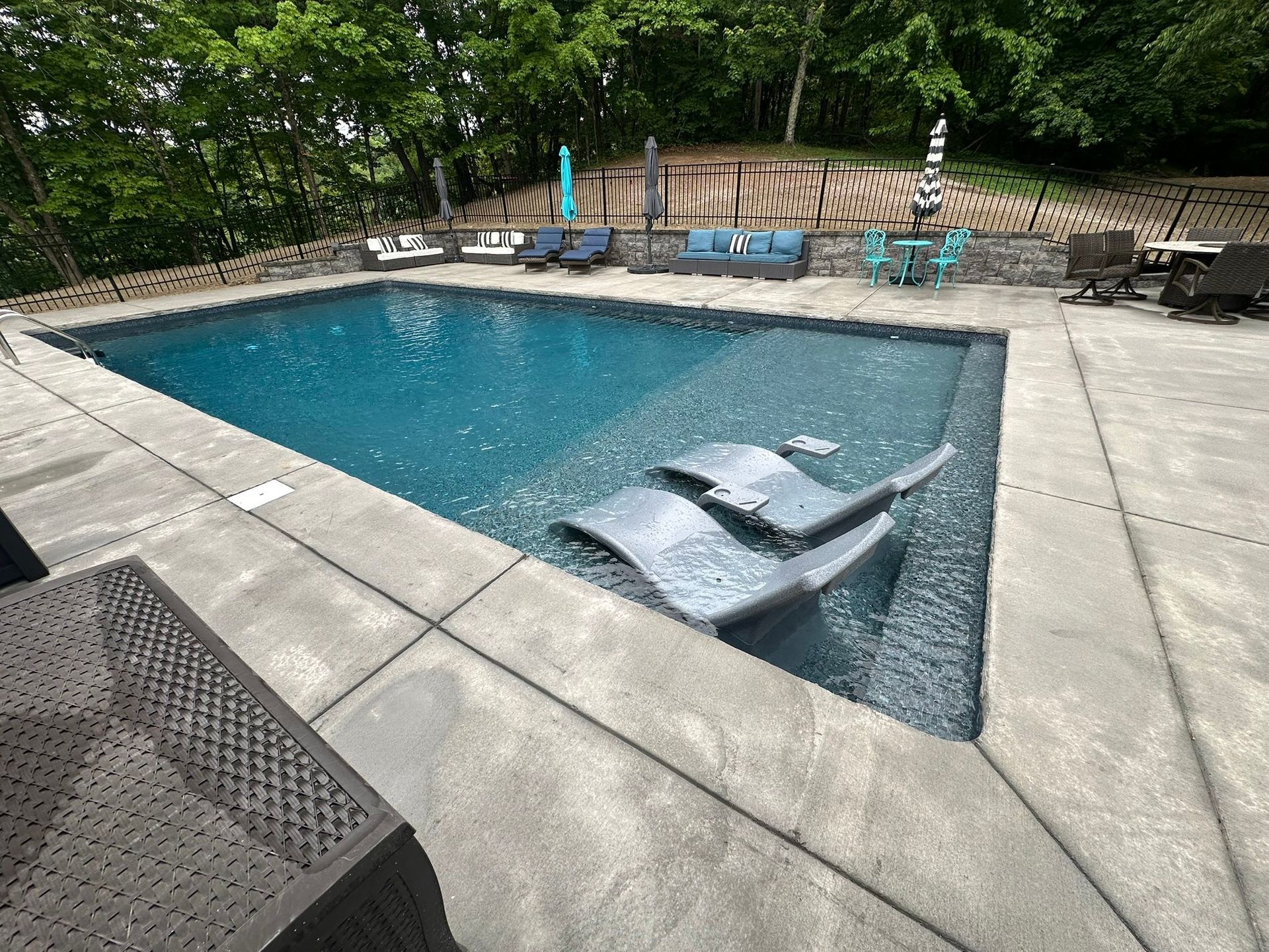Backyard swimming pool with floating lounge chairs and patio seating on a stone deck
