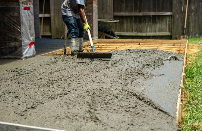 Worker smoothing fresh concrete slab with a rake in a backyard.