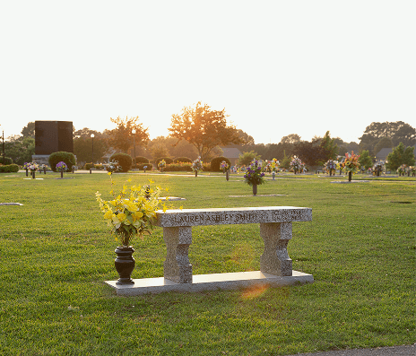 Stone bench with yellow flowers in a grassy park at sunset