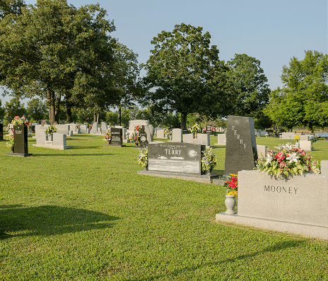 Grassy cemetery with headstones and flower arrangements under sunny green trees