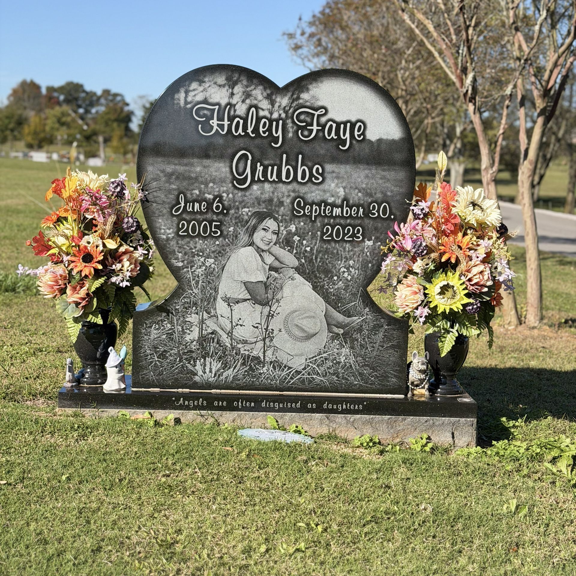 Gravestone with flowers and a photo engraving in a grassy cemetery under a clear sky