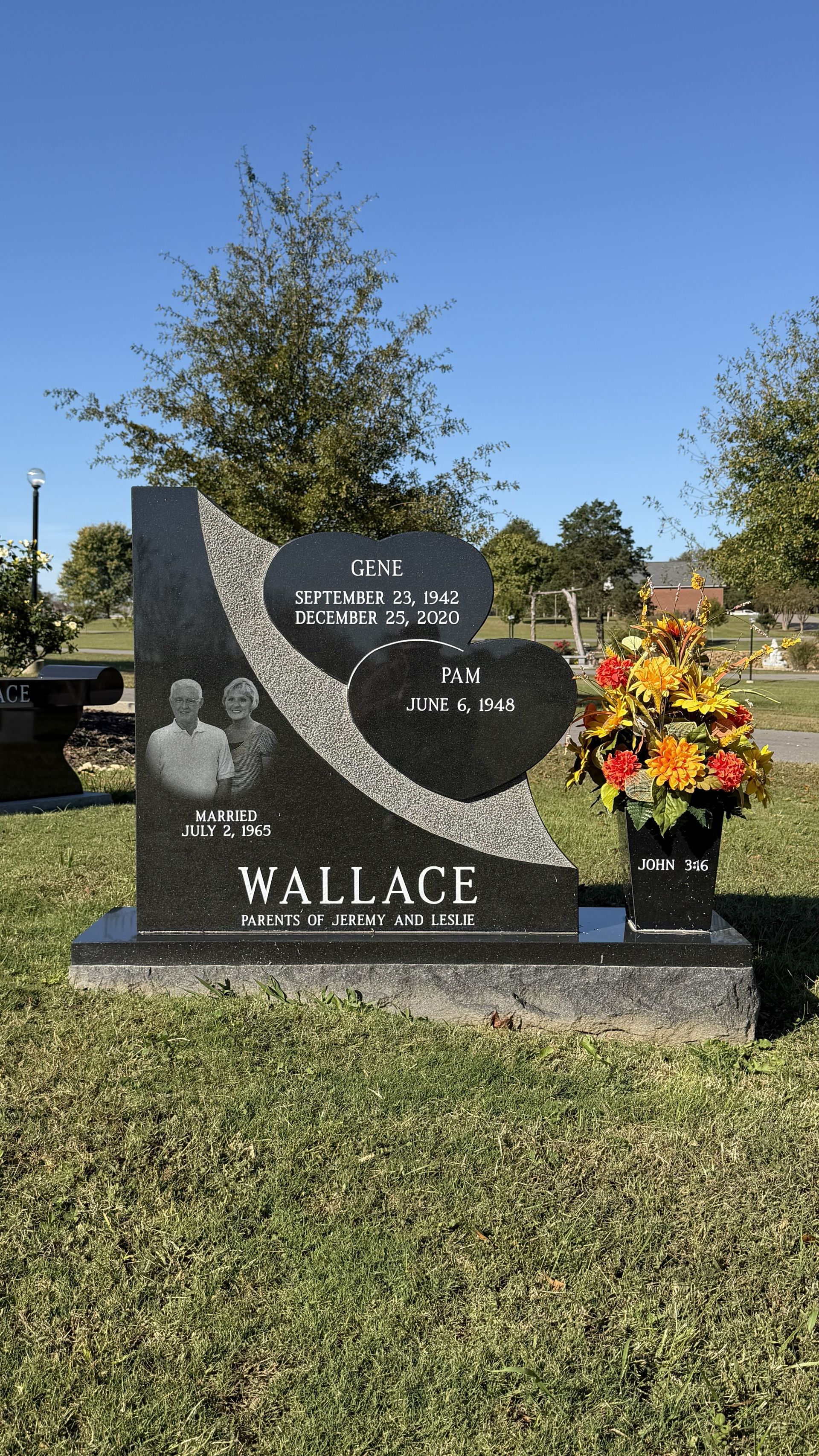 Gravestone with heart-shaped plaque reading Wallace, surrounded by flowers in a cemetery