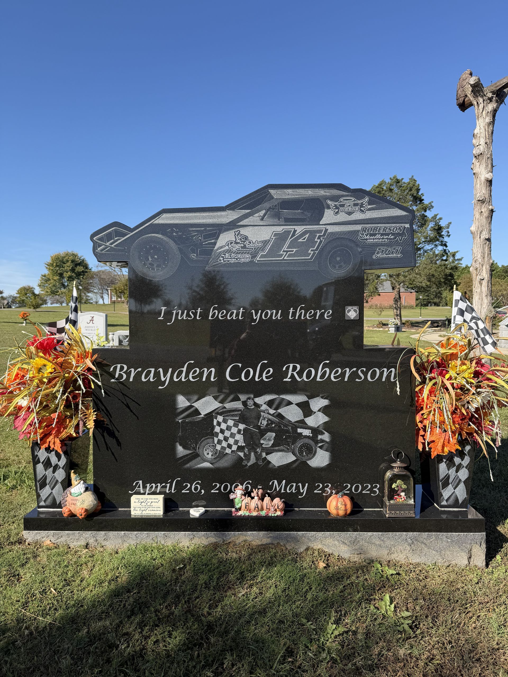 Black granite memorial gravestone with flowers and pumpkins in a sunny cemetery