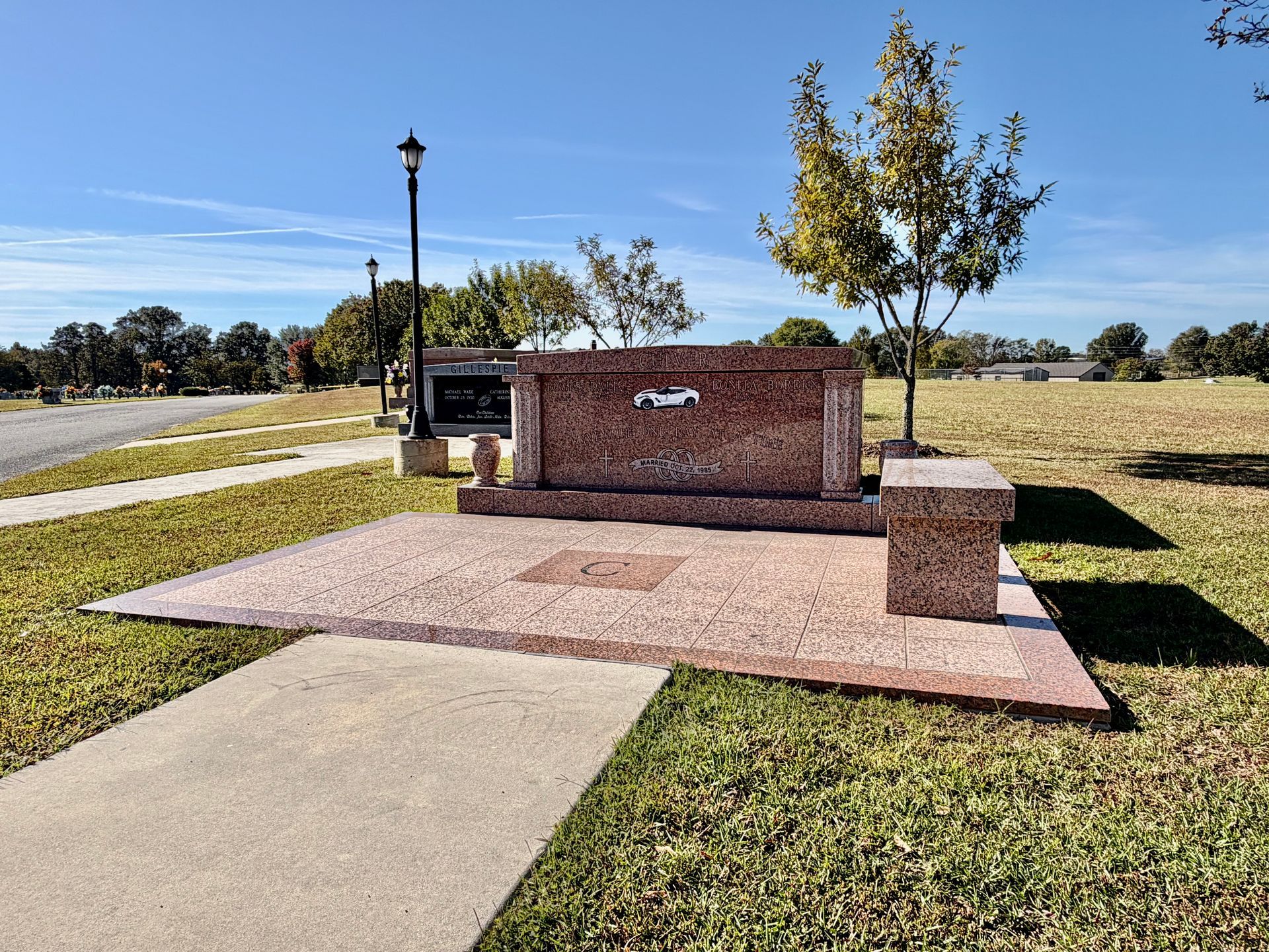 Brick park bench with plaque beside a sidewalk and grass under a sunny sky